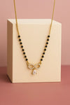 Necklace with black beads and a gold bow pendant on a beige stand against a pink background