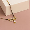 Gold necklace with black beads and a teardrop pendant on a pink surface