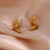 Pair of elegant gold knot earrings displayed on fabric – stylish and classy stud earrings