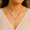 Necklace with black beads and a gold pendant on a person wearing a white top.