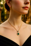 Close-up of a person wearing a gold necklace with an emerald pendant against a blurred background