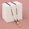 Necklace with black and gold beads and a decorative pendant on a white cube against a pink background