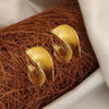 Gold leaf-shaped earrings on a textured brown surface