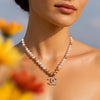 Pearl necklace with a CC logo pendant worn by a person, with blurred flowers in the foreground.