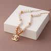 Pearl necklace with gold CC pendant on a white stand against a brown background