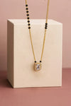 Gold necklace with a square pendant on a beige cube against a pink background