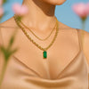 Gold chain necklace with a green pendant on a model against a blurred floral background