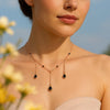 Woman wearing a delicate necklace with black teardrop pendants against a blurred natural background