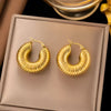 Flatlay of bold ribbed gold hoop earrings on elegant brown display background

