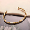 Side view of gold bamboo cuff bracelet showing elegant segmented design on soft fabric background

