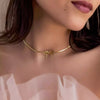Gold bow-shaped necklace worn by a person with a blurred background